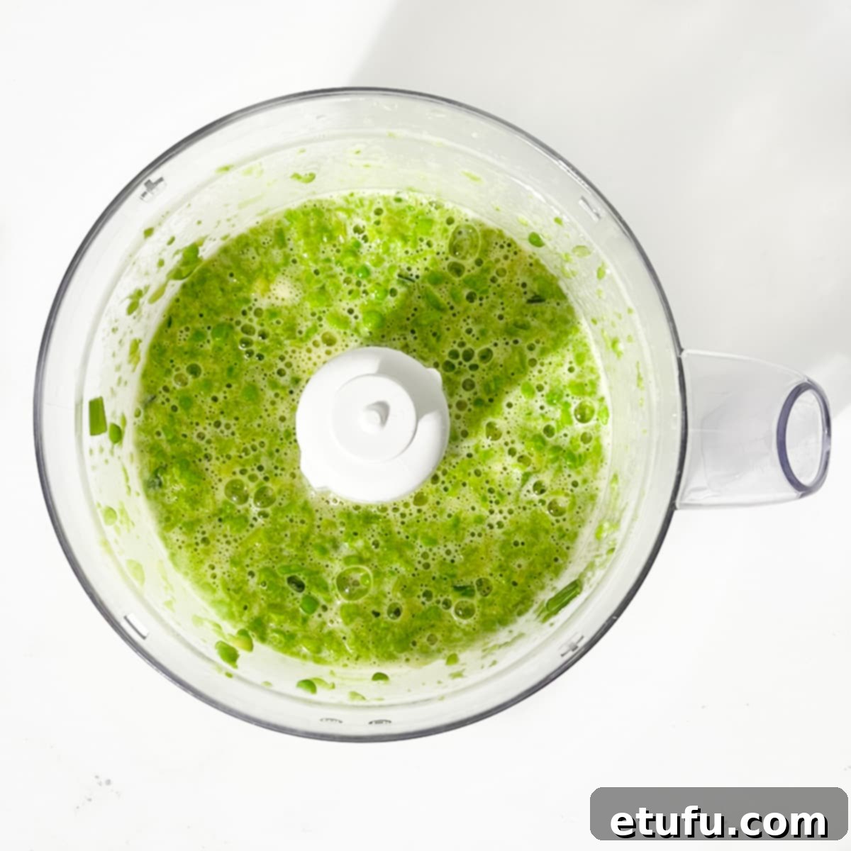 The blended mixture of peas, eggs, and spring onions inside a food processor, showing a smooth, finely chopped consistency.