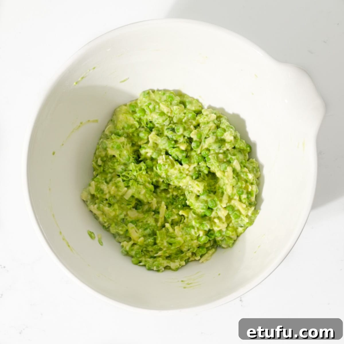 The green pea fritter mixture in a large white bowl, showing a thick batter consistency with visible whole peas and grated cheese.
