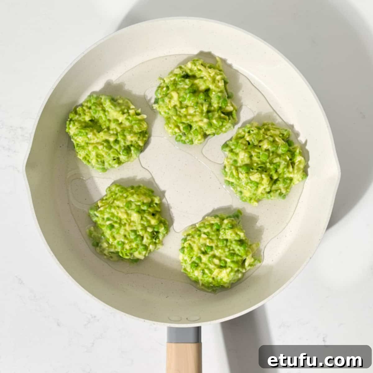 Dollops of the pea fritter batter being scooped into a large frying pan with hot oil, ready for shaping and cooking.