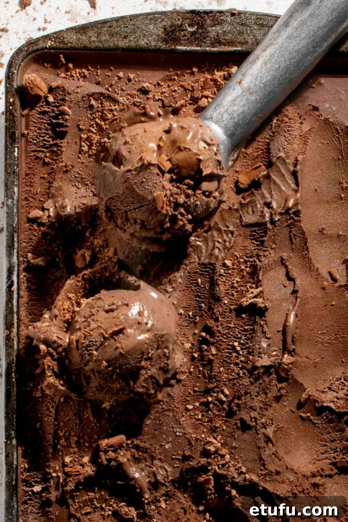 Dark chocolate ice cream in a baking tray with an ice cream scoop, ready to be served.