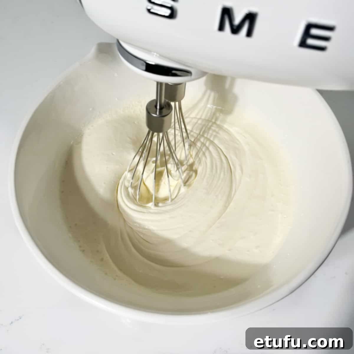 Whisking the cream in a large white bowl until stiff peaks form.