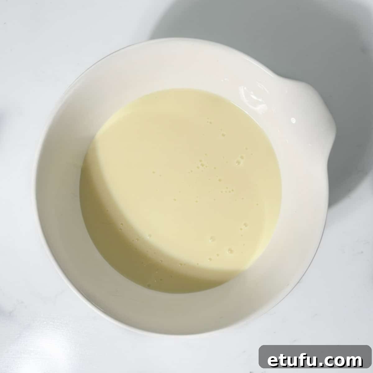 Condensed milk in a small white bowl, prepared for mixing with chocolate.