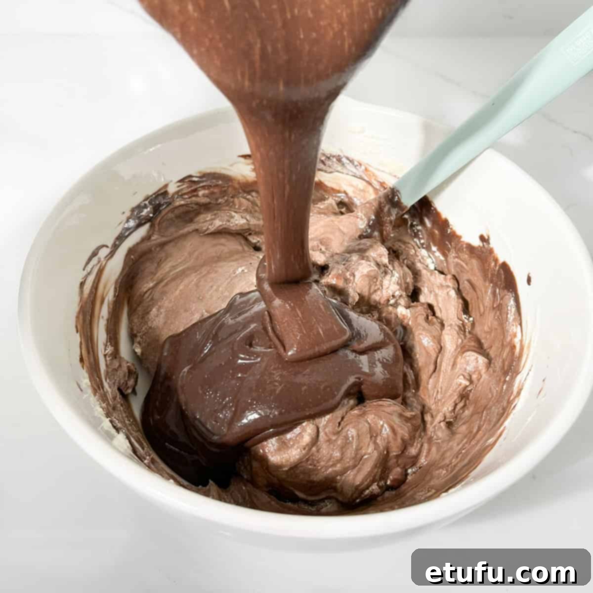 Adding the remaining chocolate mixture to the whipped cream in a large white bowl.