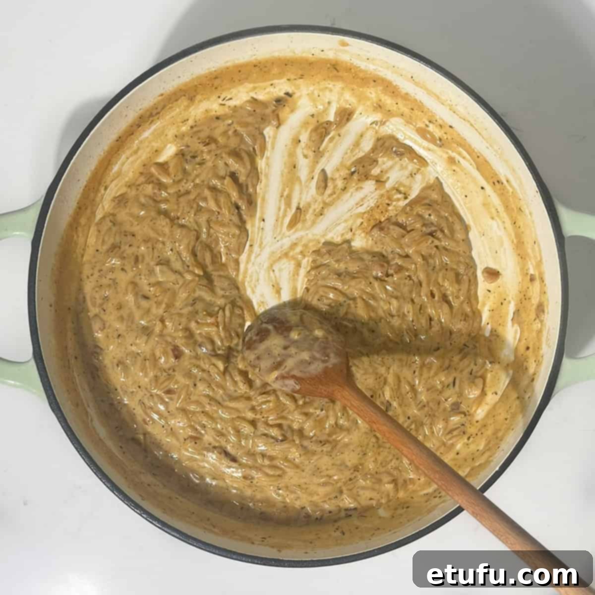 Showing the consistency of the lemon orzo pasta by dragging a wooden spoon through it, indicating readiness.