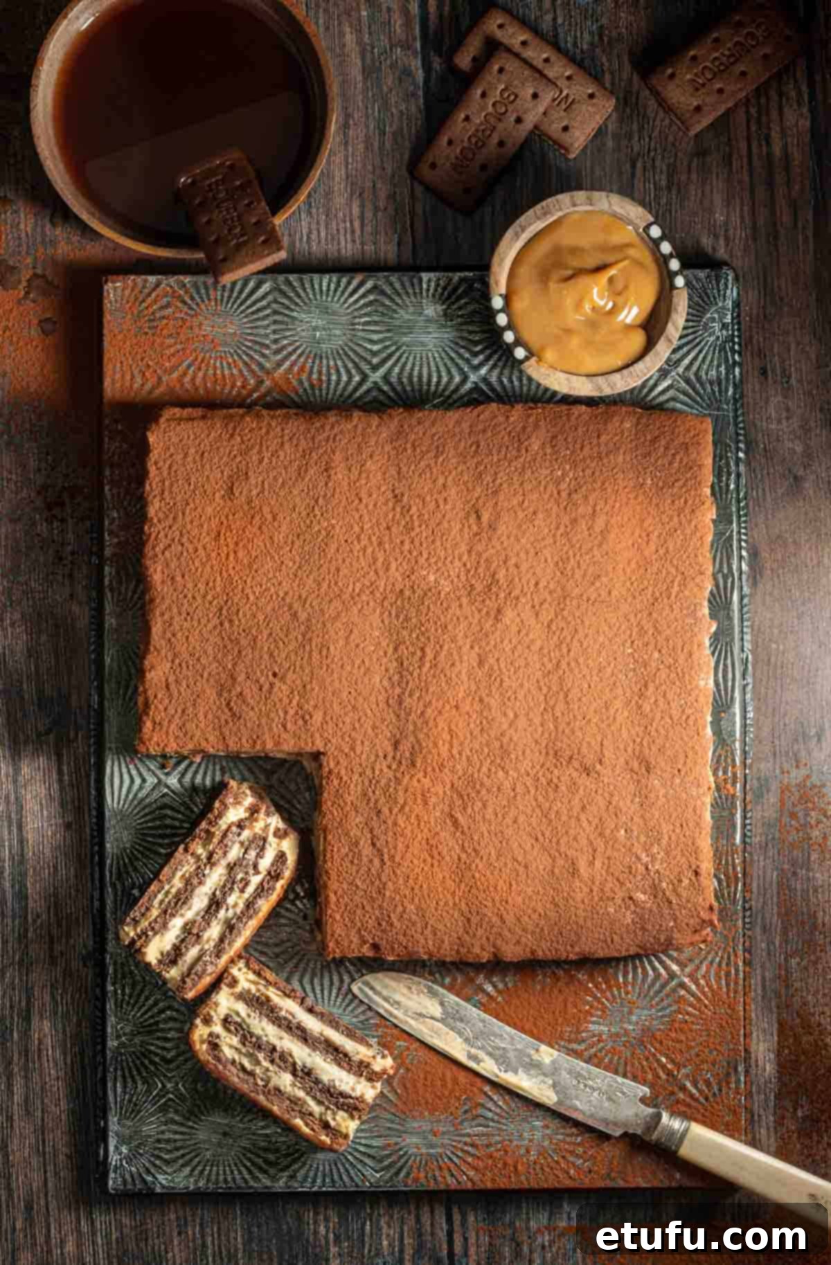 A beautifully layered Chocotorta on a metal tray with one slice removed, showcasing its rich chocolate and cream layers. This Argentinian no-bake chocolate cake is perfect for parties.