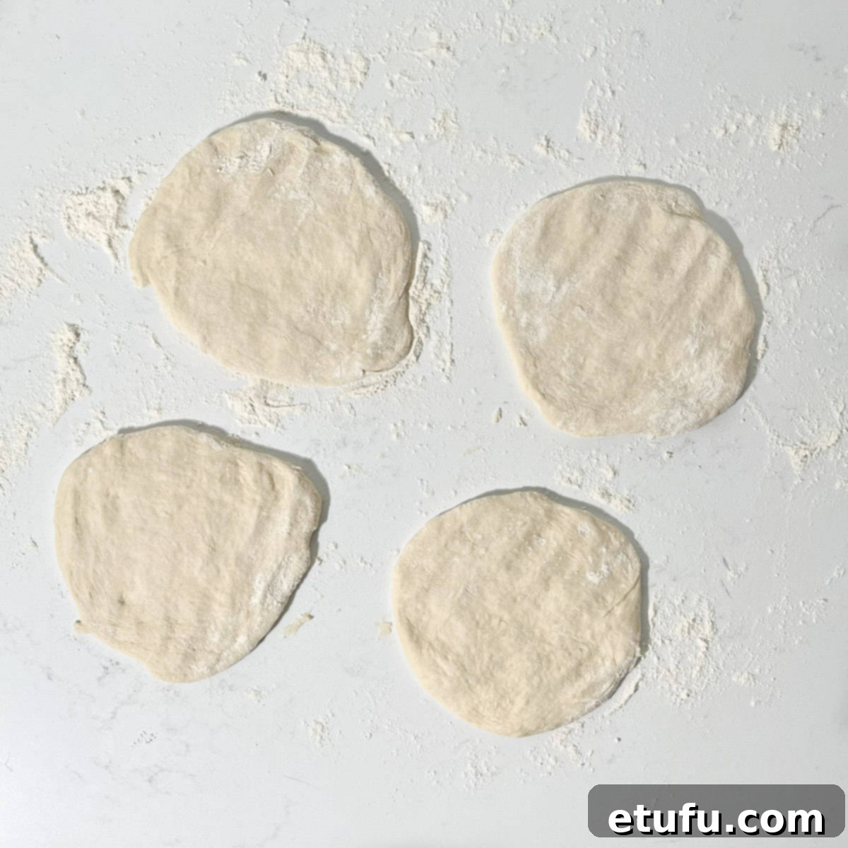 Four portions of Peshwari naan dough, with a hand flattening one into a disc shape.