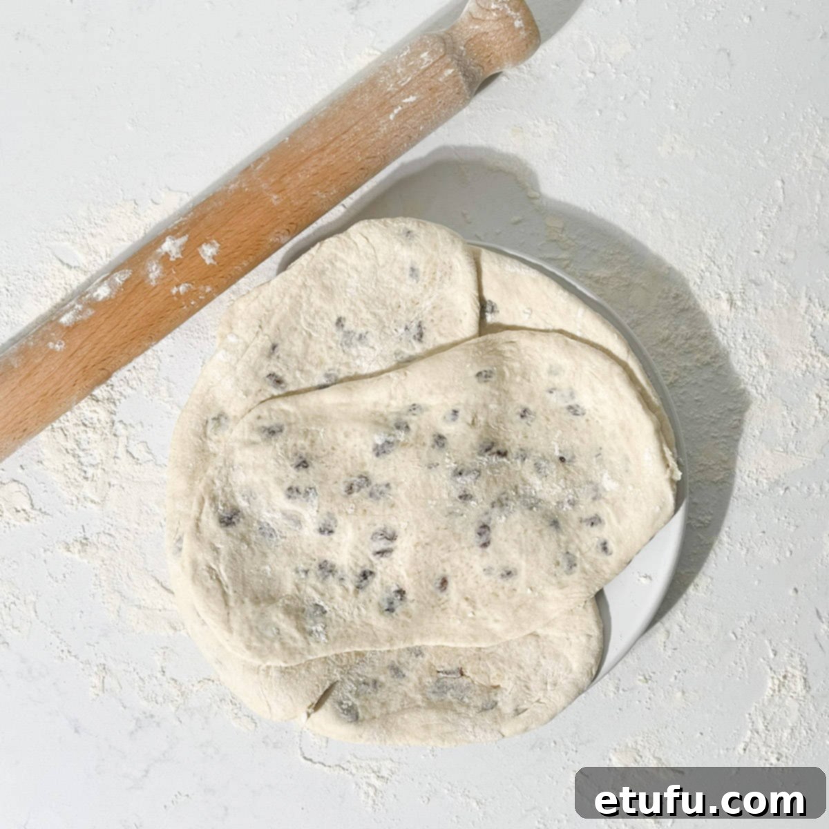 Four rolled-out Peshwari naans resting on a white plate, ready for cooking.