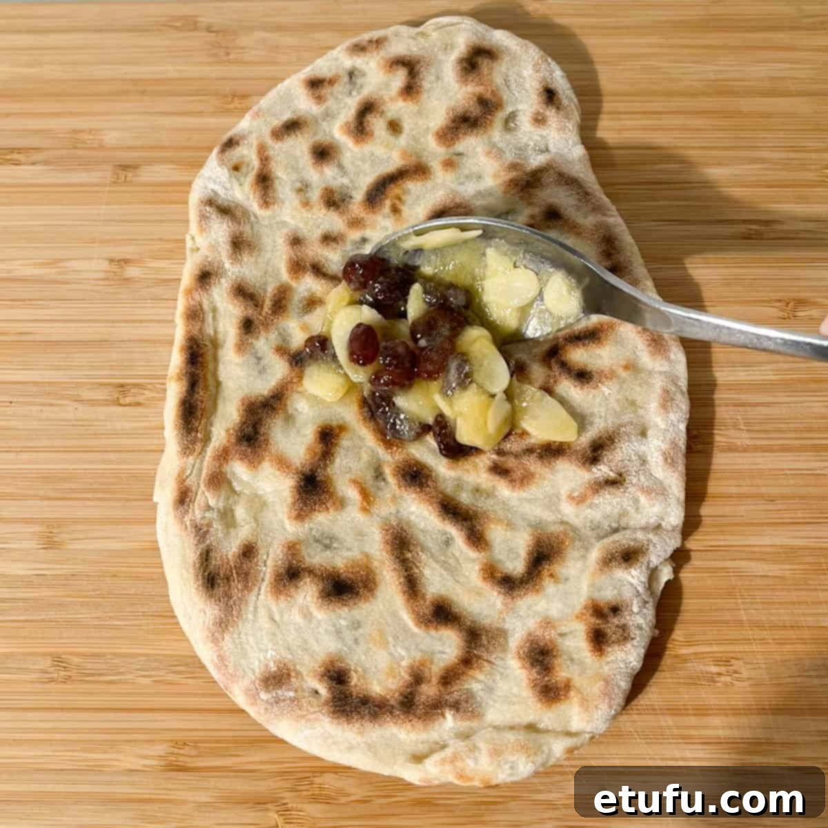 A spoonful of sweet glaze being applied to a hot Peshwari naan.
