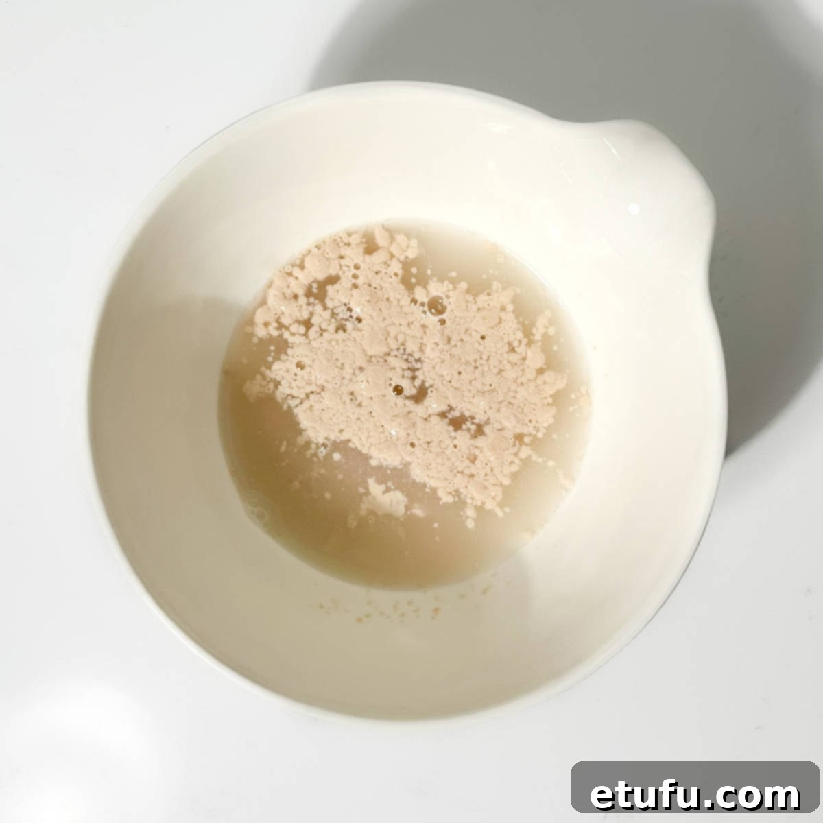 Adding dry instant yeast to lukewarm water and sugar in a small bowl.