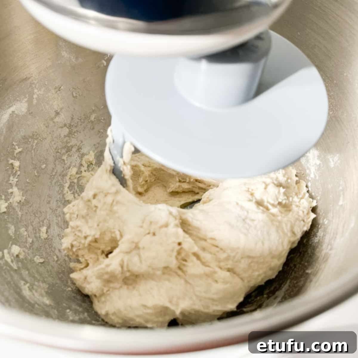 The naan dough being kneaded in a stand mixer with a dough hook.