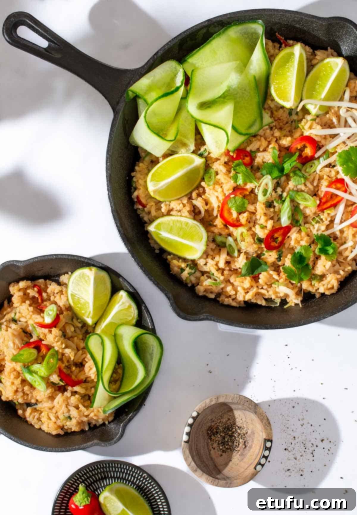 Khao pad in a black frying pan with cucumber ribbons and lime wedges.