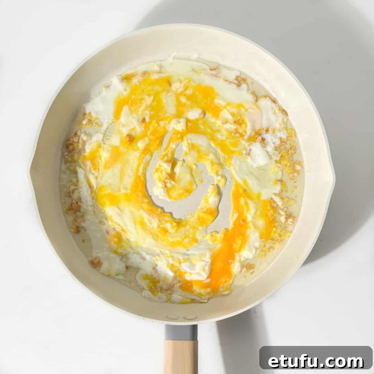 Breaking the eggs up in the pan.