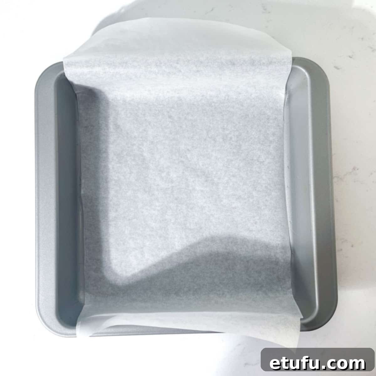 A square pan prepared with parchment paper for the fudge.