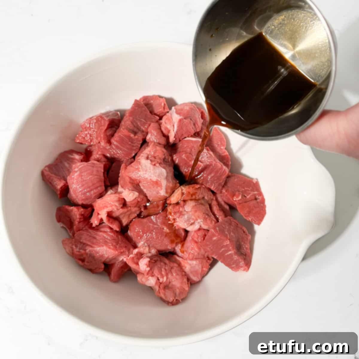 Pouring Worcestershire sauce over the cubed rump steak.
