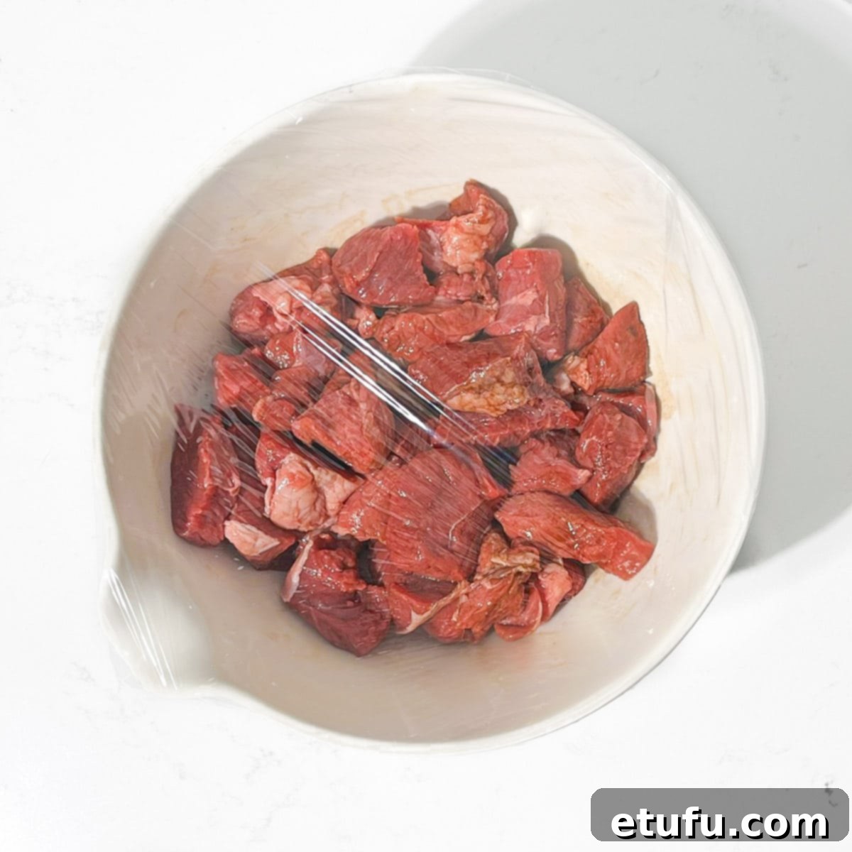 Covering the marinating meat with plastic wrap.