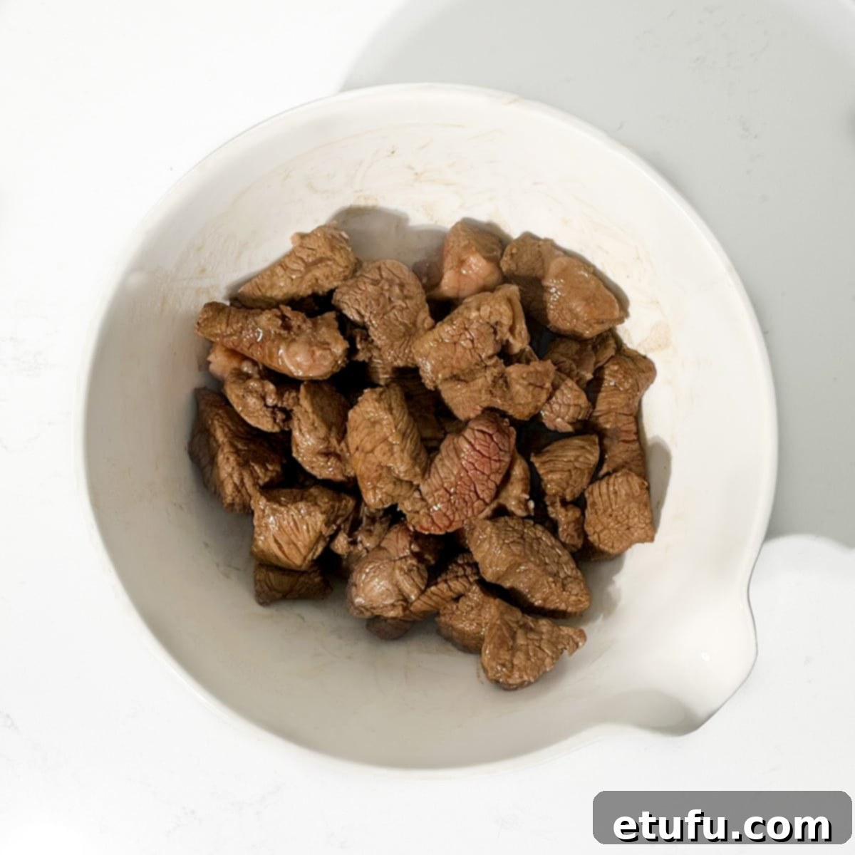 Browned meat in a large white bowl.