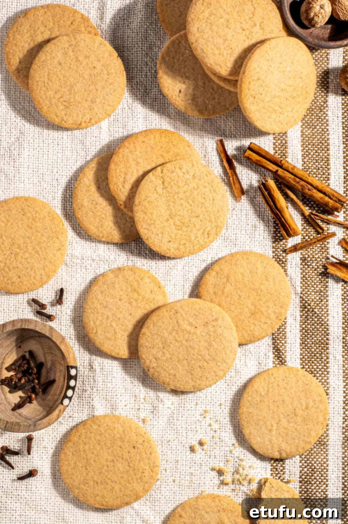 Outydse soetkoekies scattered across a textured tea towel, surrounded by nutmeg, cloves and cinnamon sticks.