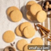 Outydse soetkoekies scattered across a textured tea towel, surrounded by nutmeg, cloves and cinnamon sticks.