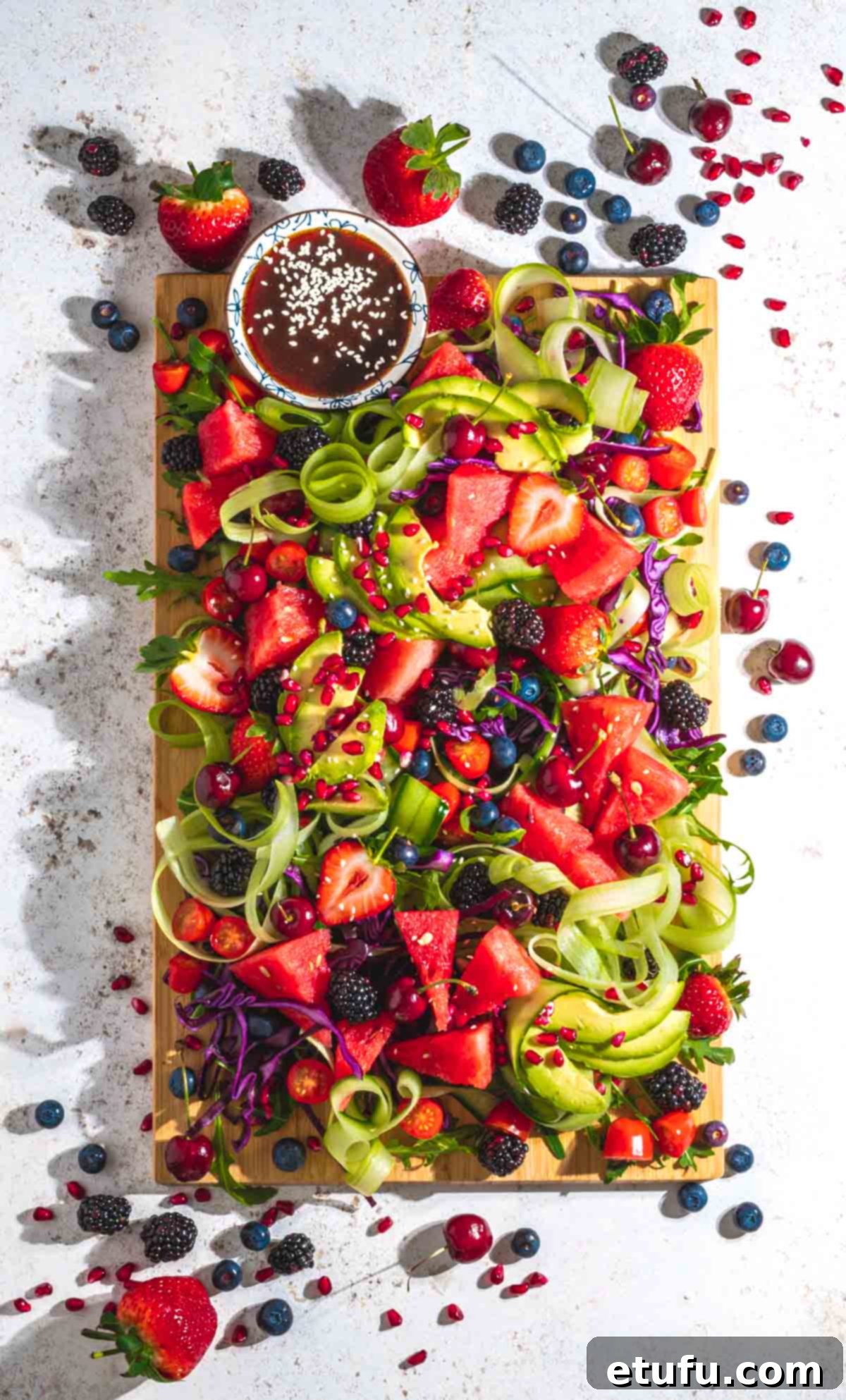A beautifully arranged rainbow salad on a rustic wooden board, set against a clean white background.