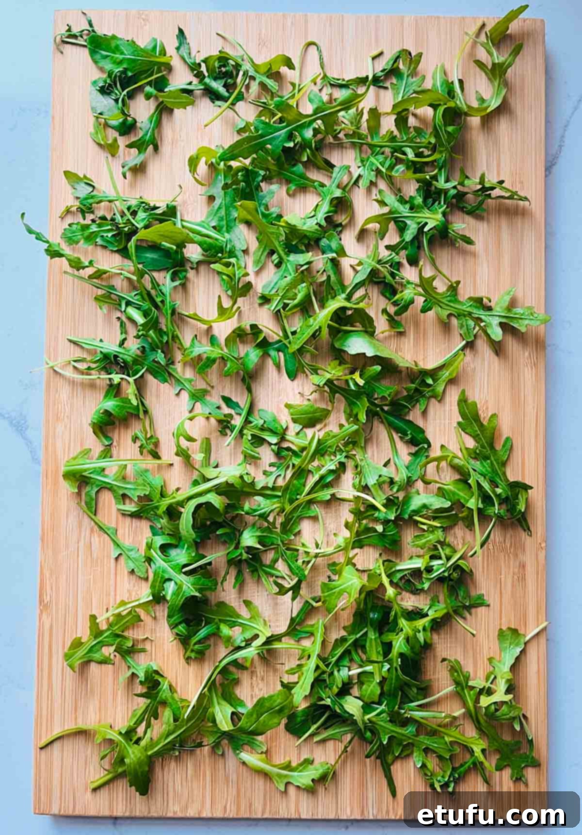 Fresh rocket leaves scattered on a rustic wooden board, forming the base of the salad.