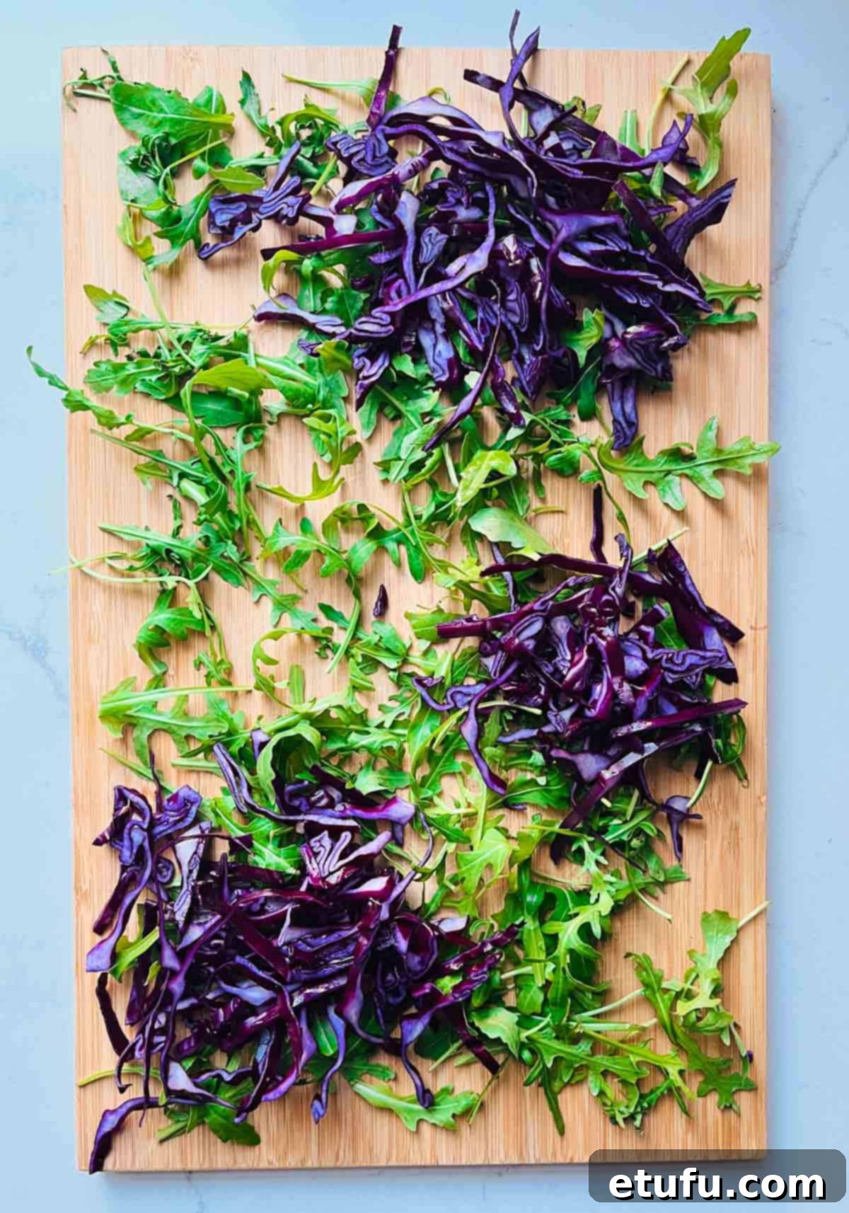 Rocket leaves and finely chopped red cabbage arranged in piles on a wooden board.