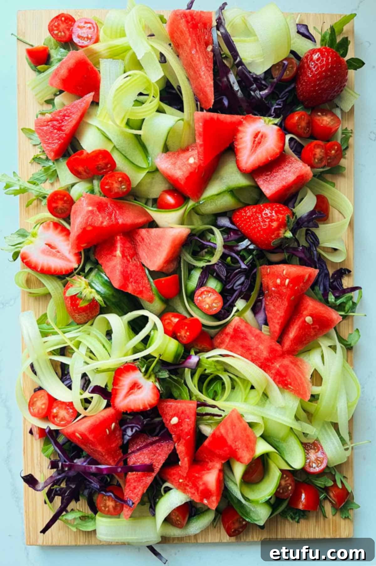 Rainbow salad with rocket, red cabbage, celery and cucumber, watermelon, now adorned with halved strawberries and cherry tomatoes.