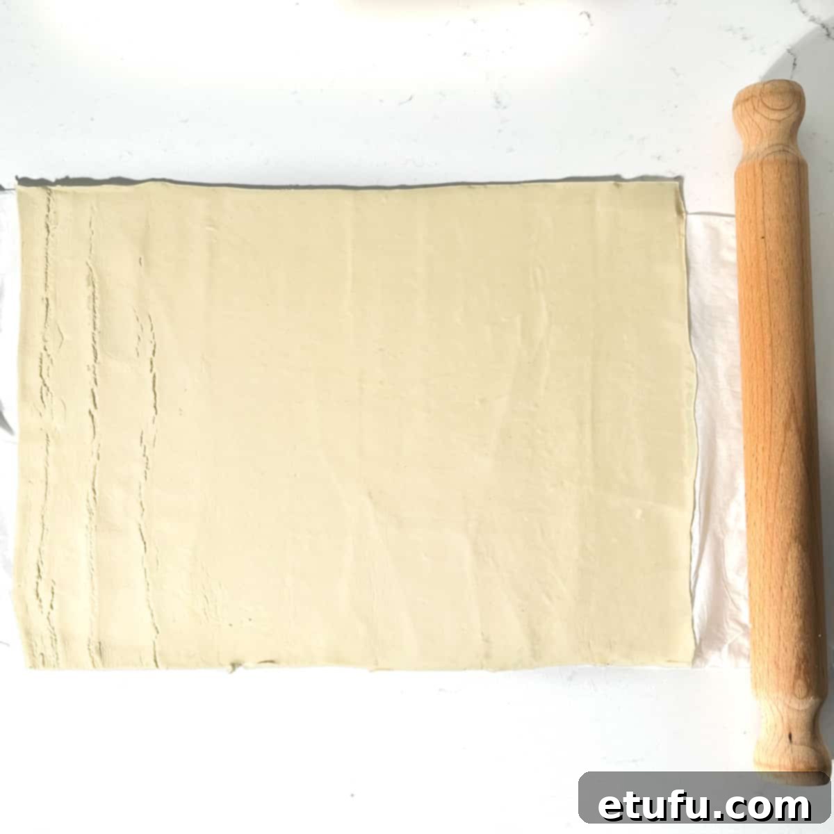 A sheet of puff pastry unrolled and slightly expanded on a kitchen countertop, ready for cutting.