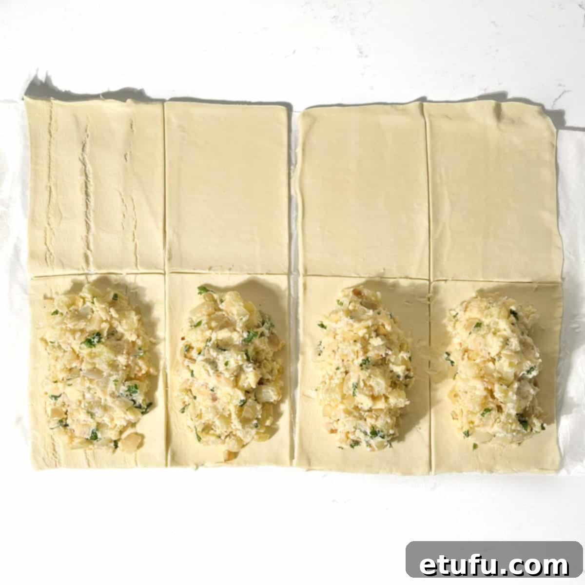 Four puff pastry rectangles with dollops of cheese and onion filling on one side of each.