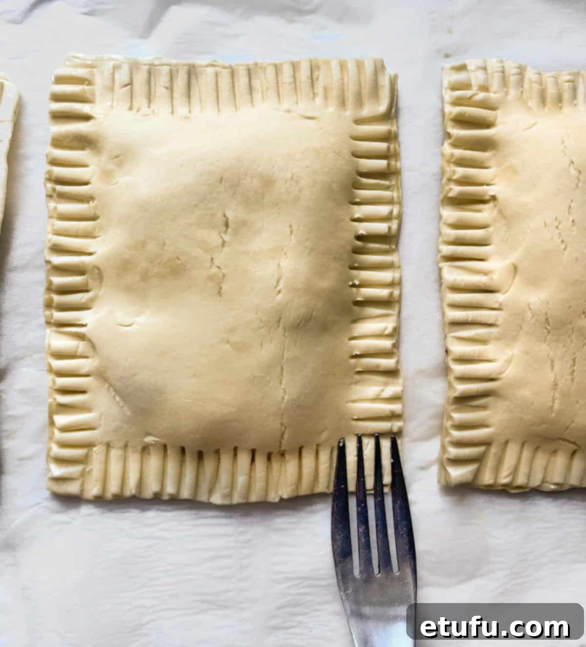 A fork being used to crimp and seal the edges of cheese and onion pasties, creating a decorative and secure seal.