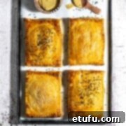 Four golden-brown cheese and onion pasties on a baking sheet, with a small bowl of mustard on the side.