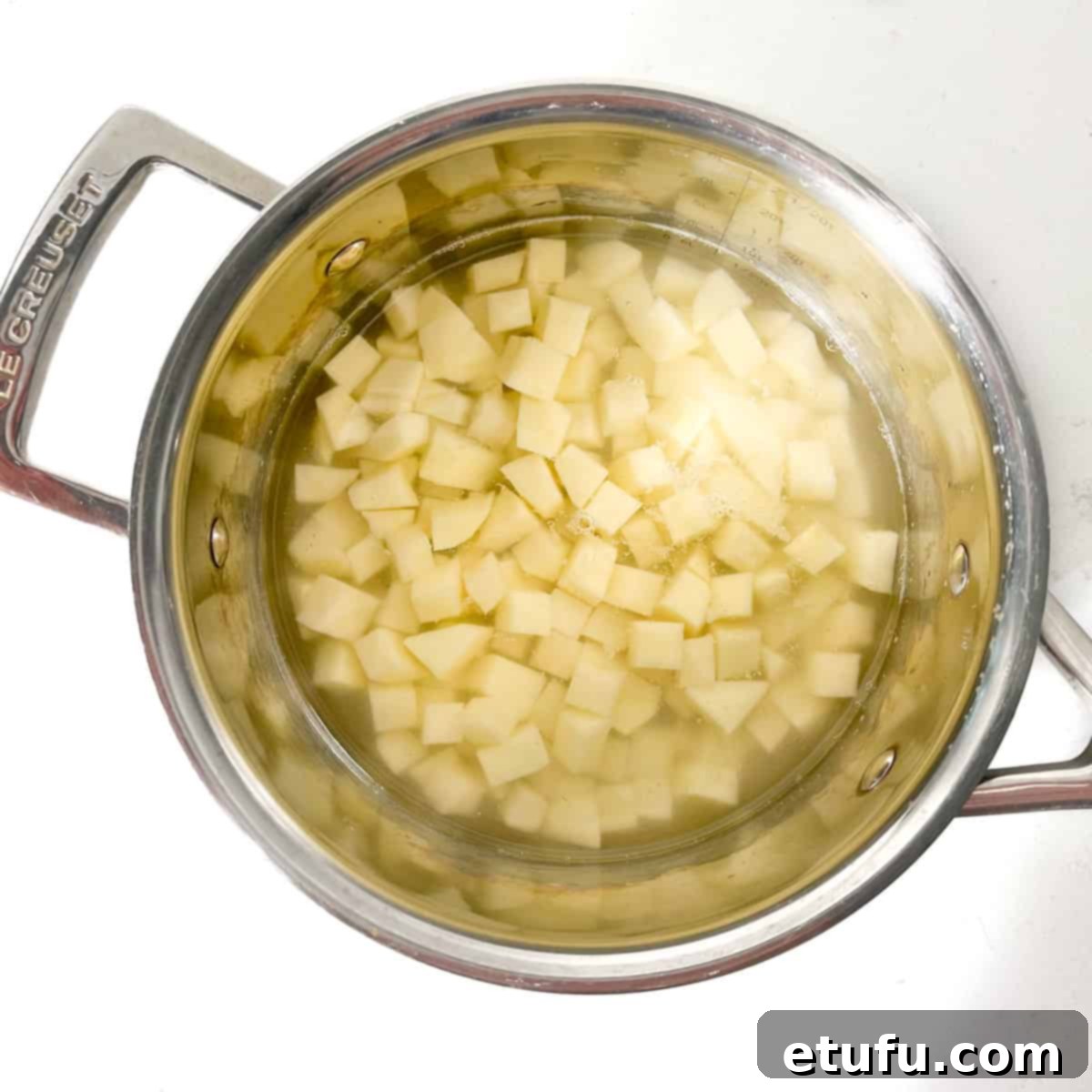 Diced potato cubes in a saucepan, covered with cold water, ready for parboiling.