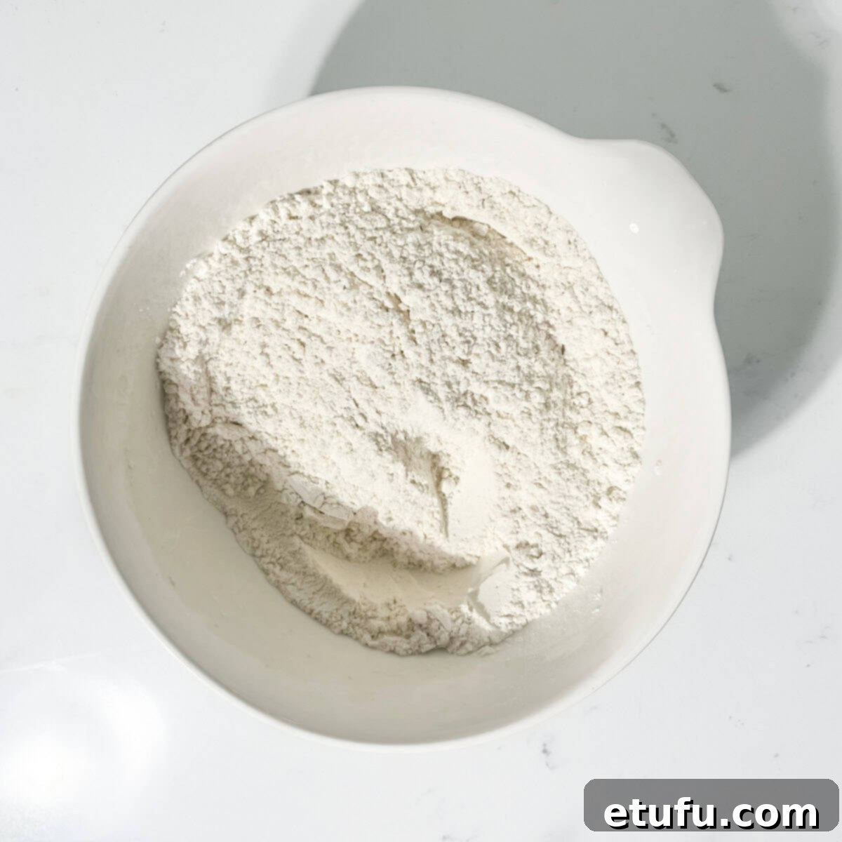 A large white bowl containing the dry ingredients for chocolate chip cookies, including flour and bicarbonate of soda.