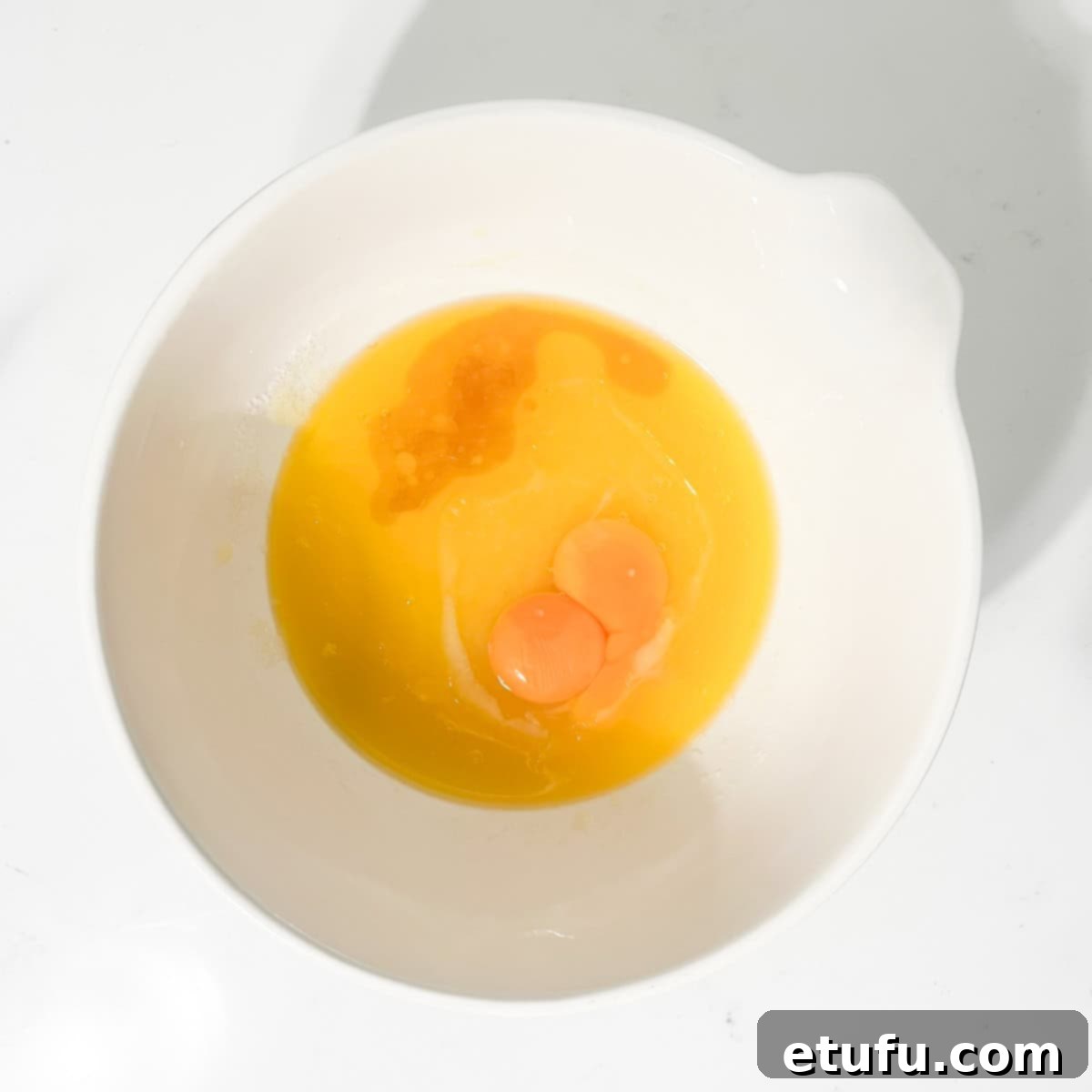 Adding eggs and vanilla extract to the butter and sugar mixture in a large white bowl.