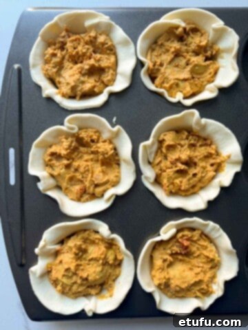 Butter chicken pies filling scooped into the pastry cases in a muffin tin.