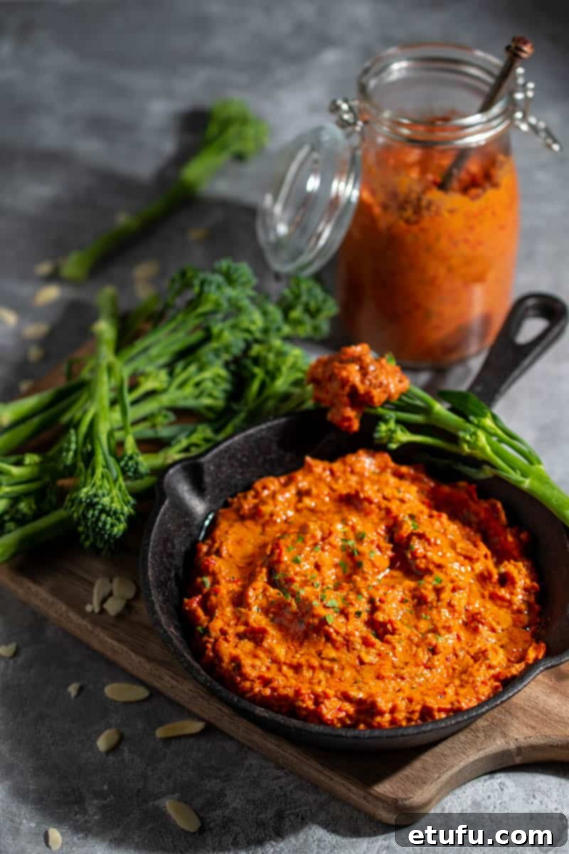 Romesco dip in a small black pan surrounded by broccoli spears, with a bottle of sauce in the background.