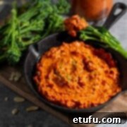 Romesco dip in a small black pan surrounded by broccoli spears, with a bottle of sauce in the background.
