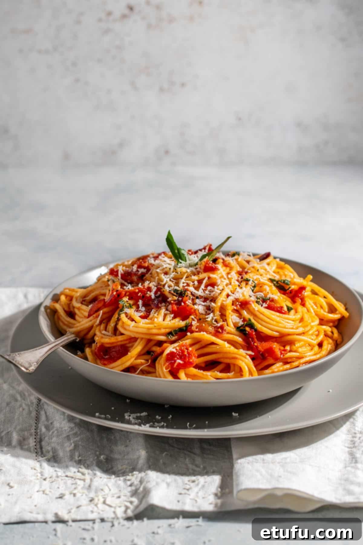Spaghetti arrabiata in a grey bowl on a white napkin, perfectly garnished and ready to serve.