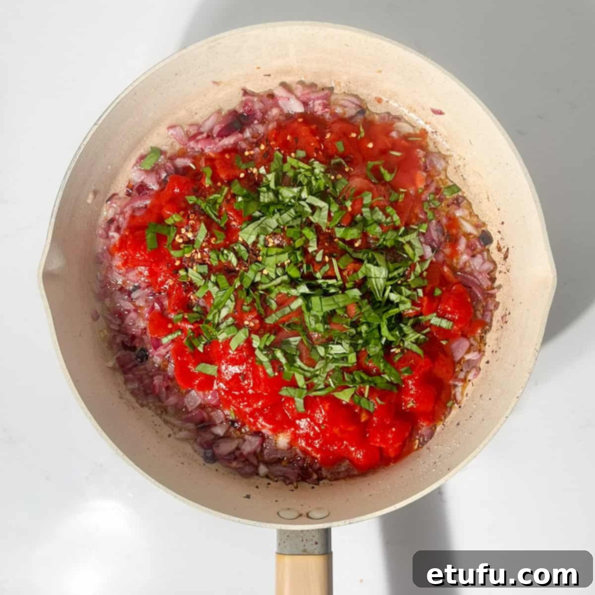 Fresh basil being added to the simmering tomato sauce in the frying pan.