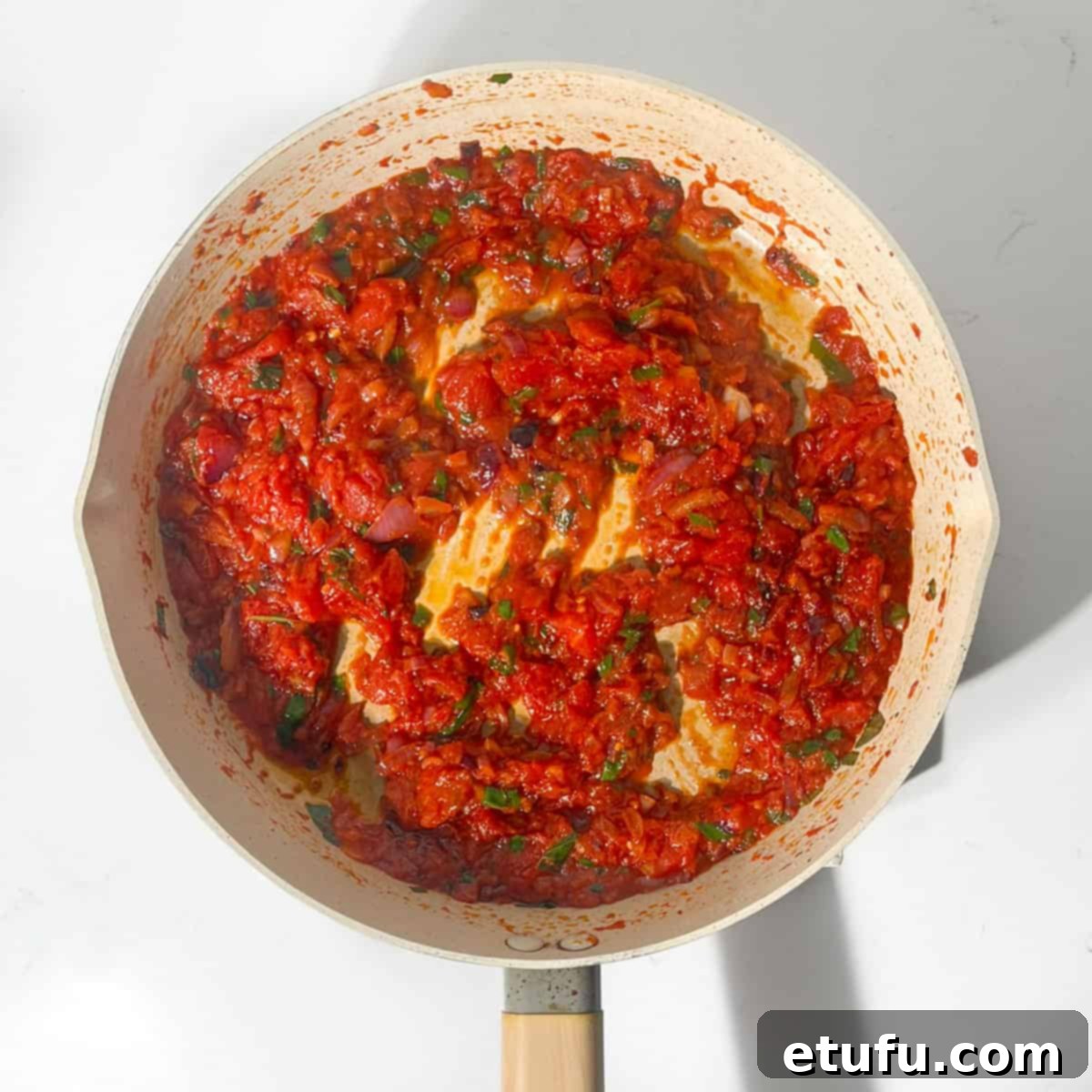 The rich, red Arrabiata sauce simmering in a large frying pan, having reduced and thickened.