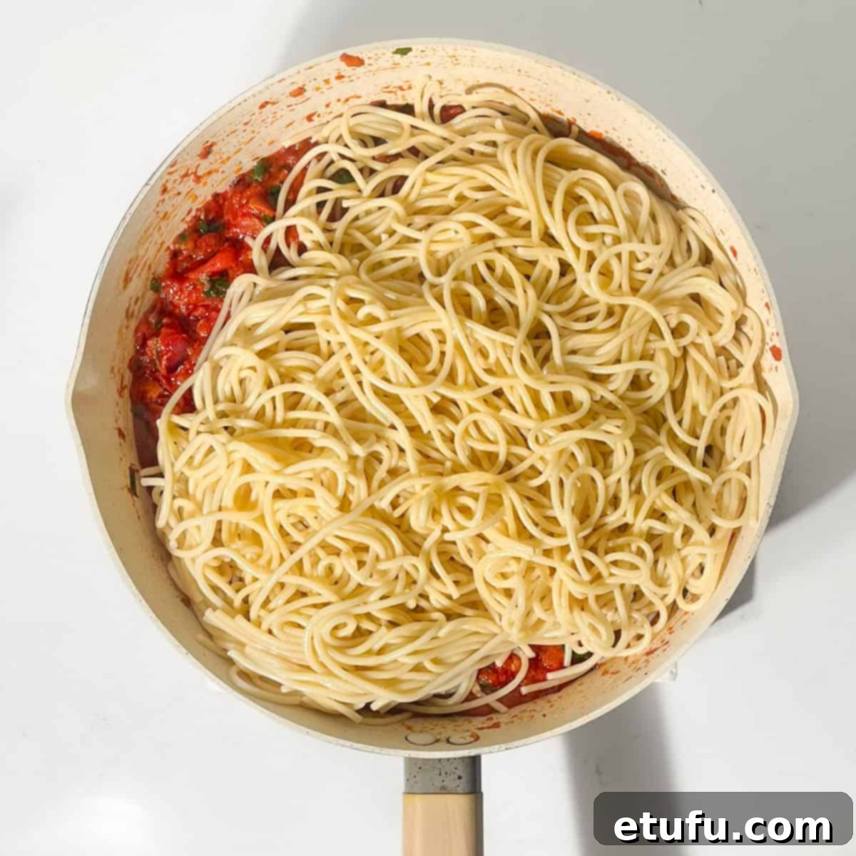 Cooked spaghetti being tossed into the Arrabiata sauce in a large frying pan.