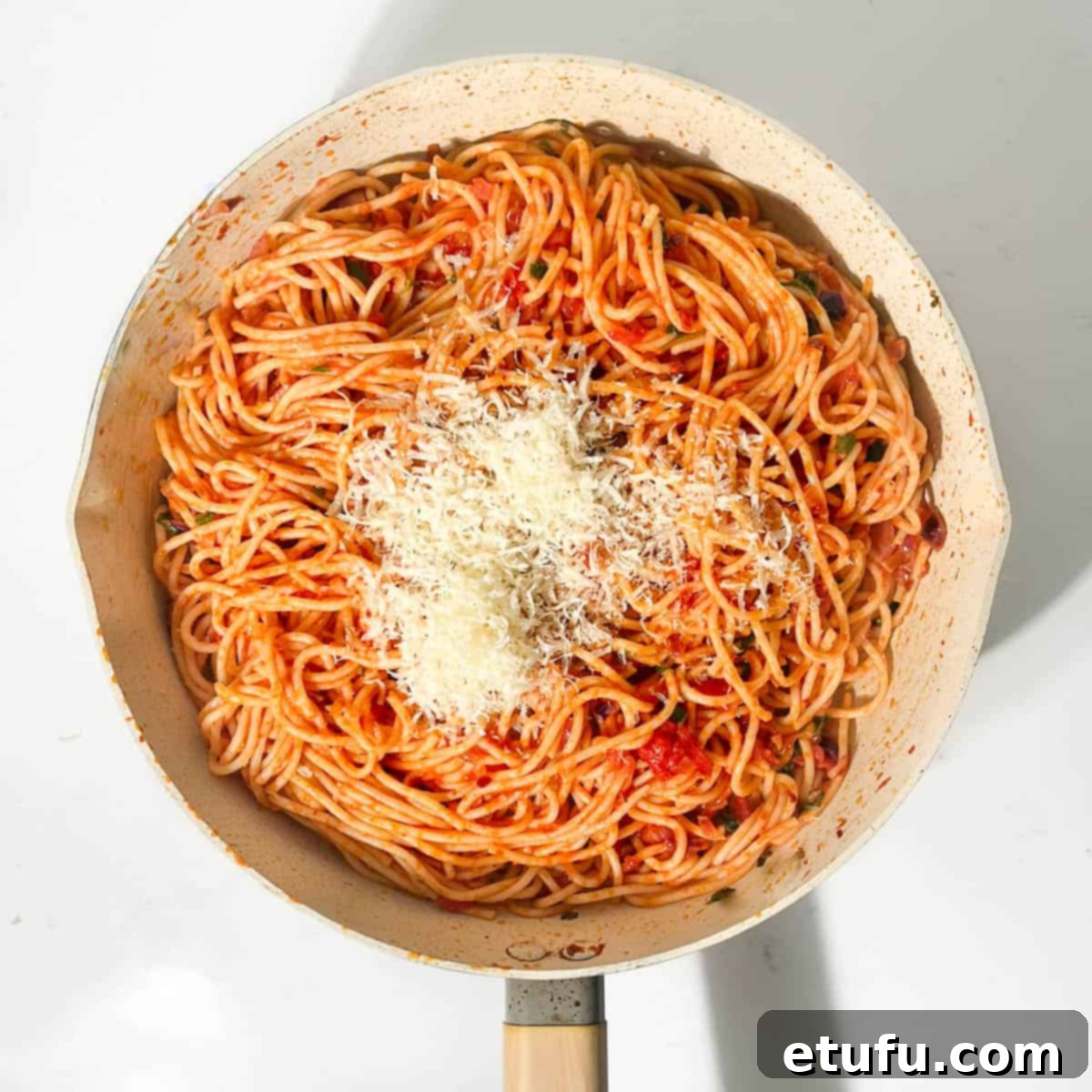 Spaghetti arrabiata in a frying pan, topped with grated parmesan cheese and fresh basil.