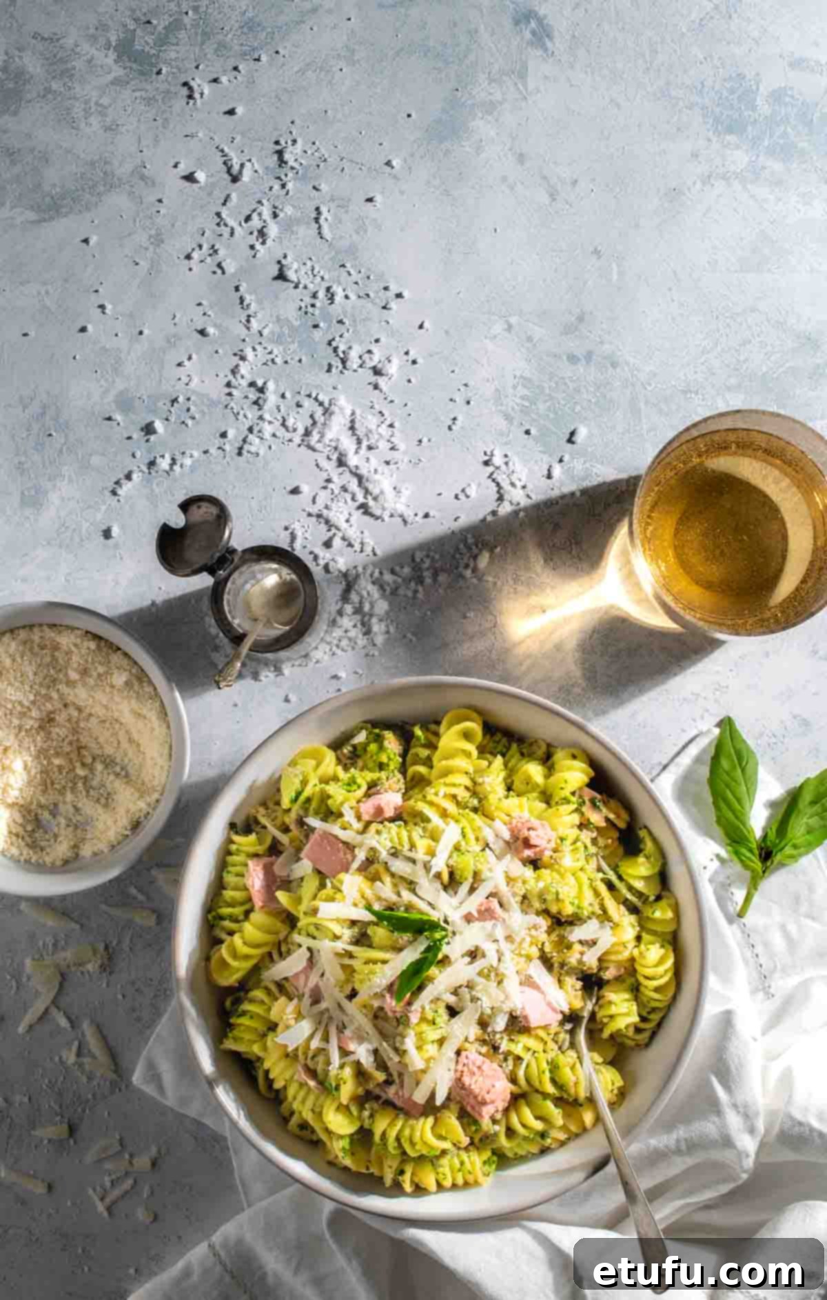 Tuna pesto pasta in a white bowl with a bowl of parmesan and a drink.