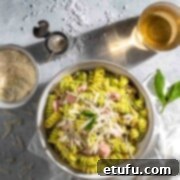 Tuna pesto pasta in a white bowl with a bowl of parmesan and a drink.