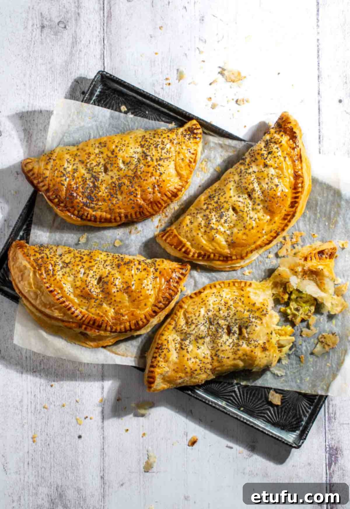 Golden Flaky Creamy Chicken Leek Pies 2 Four golden-brown creamy chicken and leek pies on a baking sheet, one cut open to reveal the rich filling.