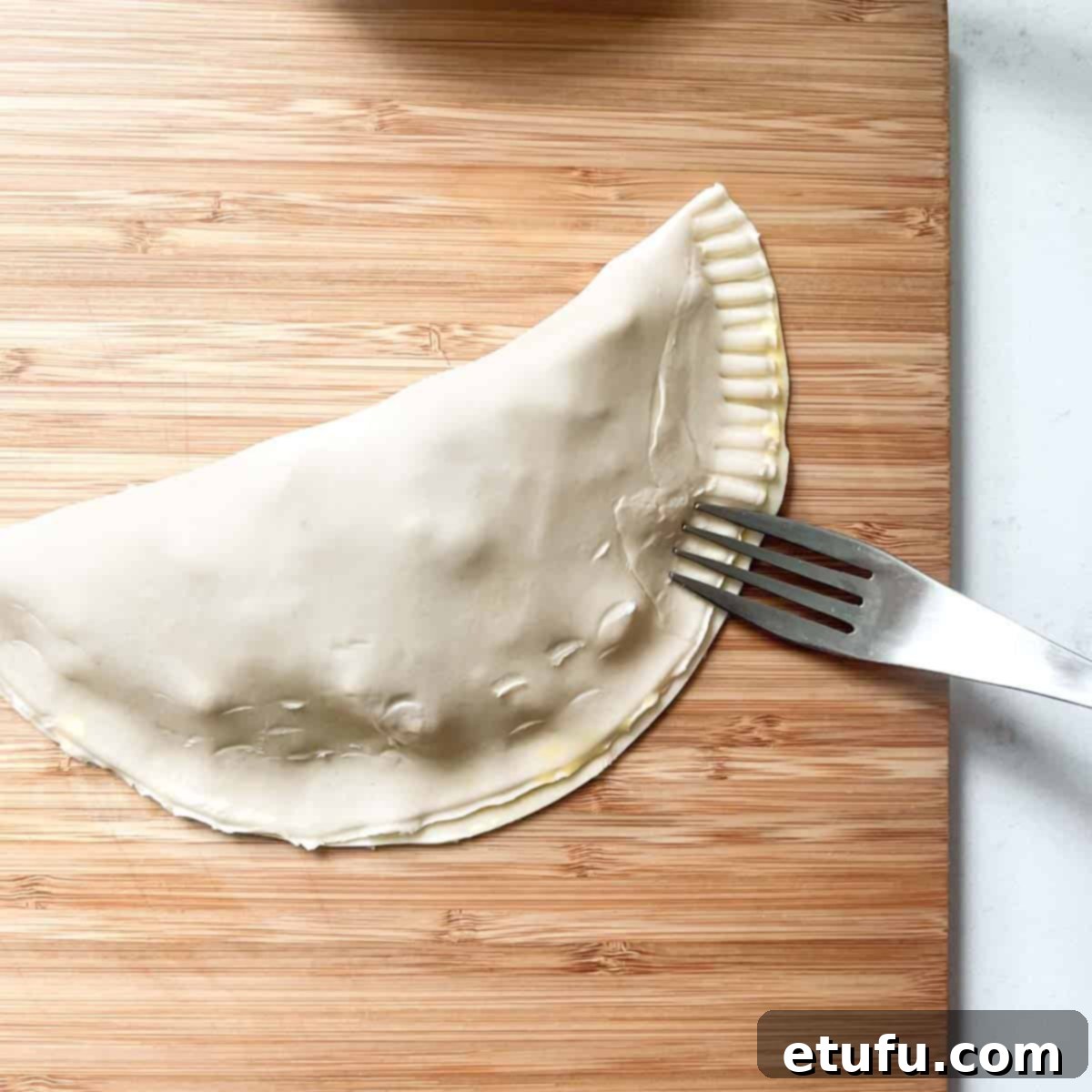 Golden Flaky Creamy Chicken Leek Pies 16 A chicken and leek pie being sealed by crimping the edges with a fork.