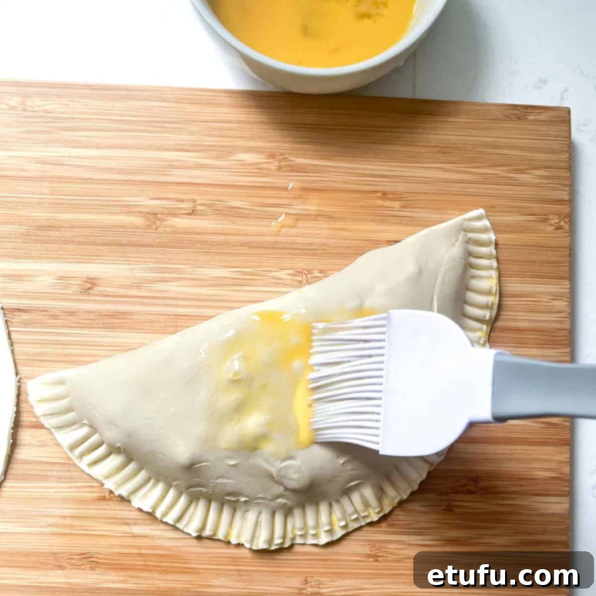 Golden Flaky Creamy Chicken Leek Pies 17 The top and sides of a chicken and leek pie being brushed with egg wash for a golden finish.