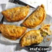 Golden Flaky Creamy Chicken Leek Pies 21 Four creamy chicken and leek pies on a baking sheet, with one pie broken open to show the filling.