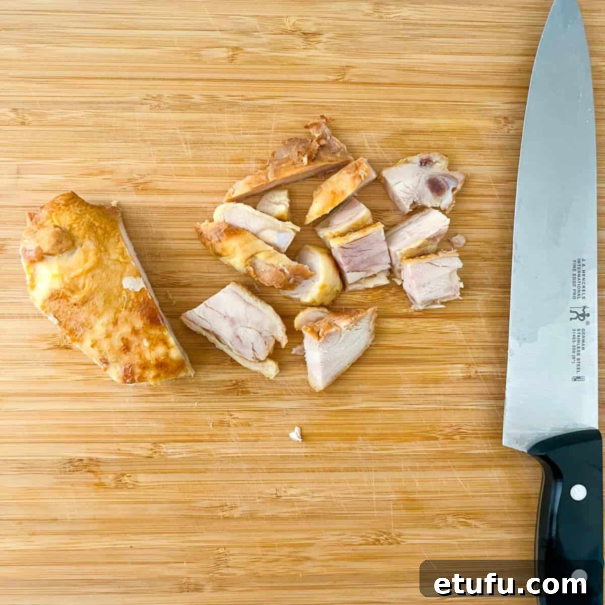 Golden Flaky Creamy Chicken Leek Pies 5 Chopping cooked roasted chicken thighs on a wooden chopping board into bite-sized pieces.