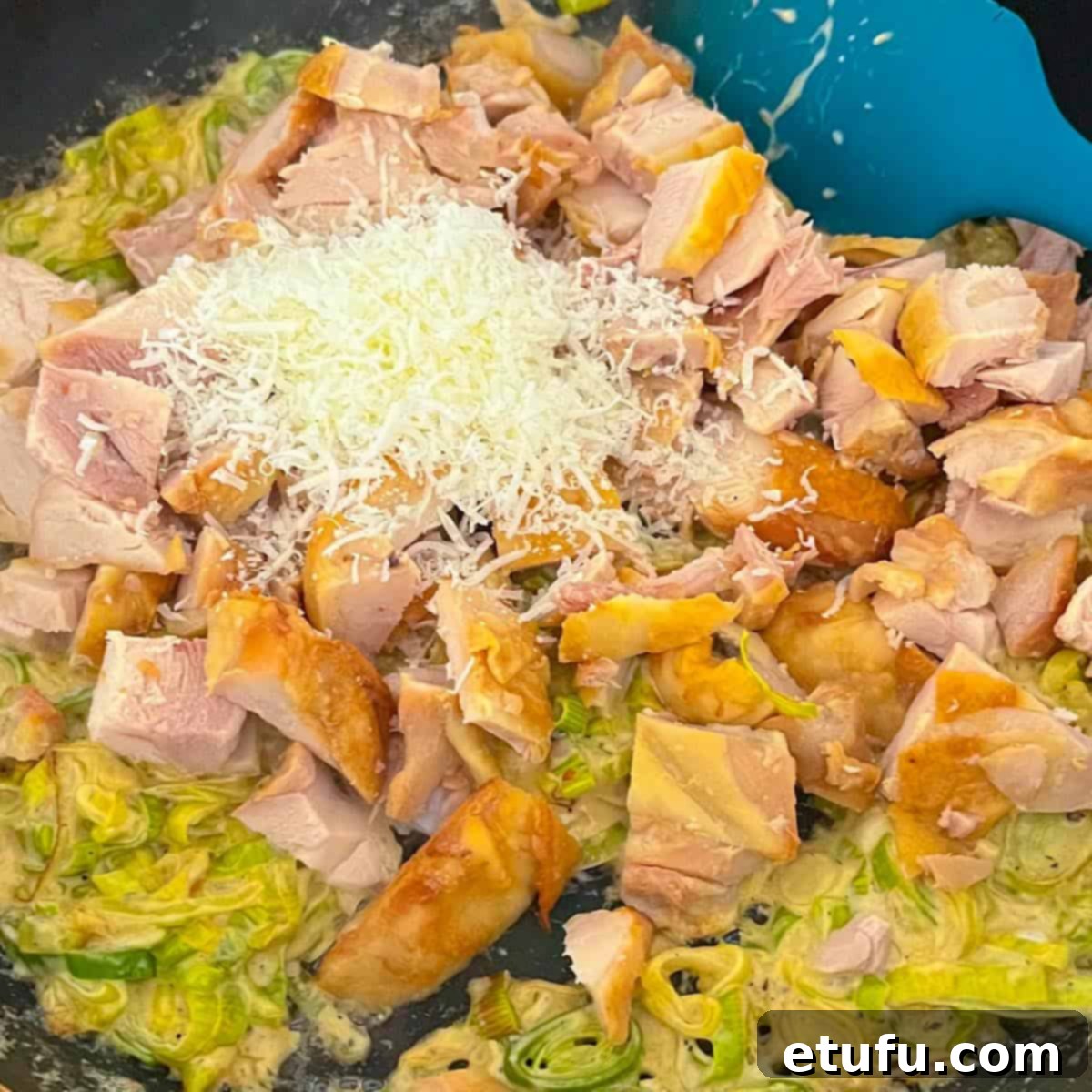 Golden Flaky Creamy Chicken Leek Pies 9 Adding chopped roast chicken and grated parmesan cheese to the leek and cream mixture in a pan.