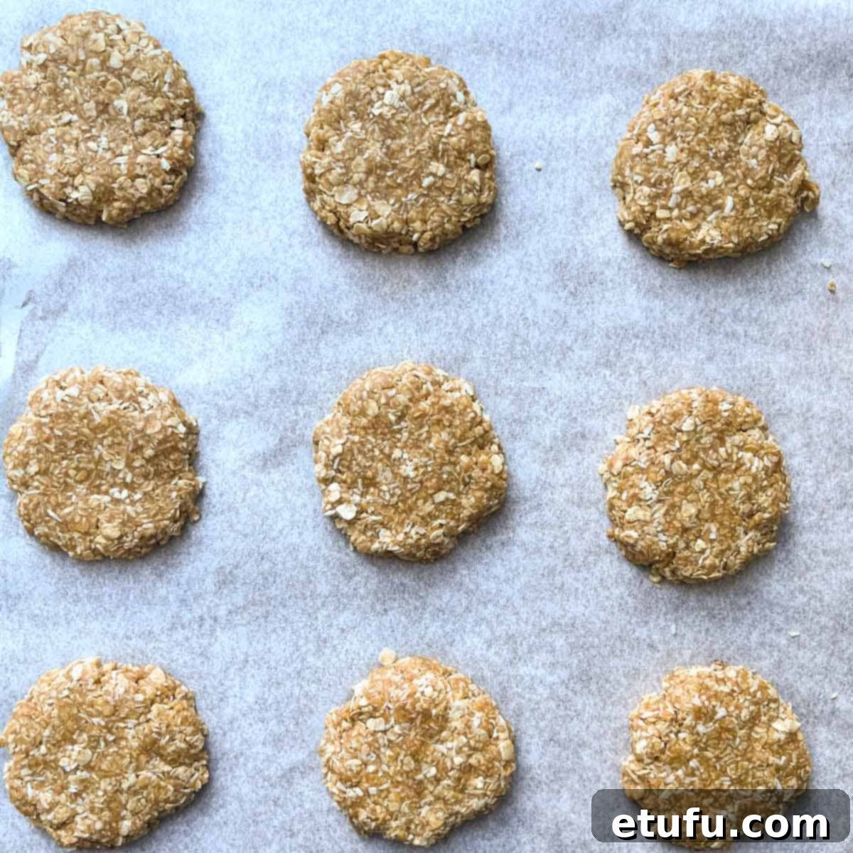Flattened coconut biscuit dough balls on a baking tray.